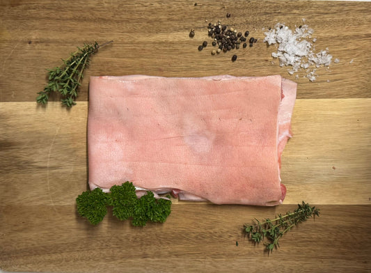 Raw pig skin on a wooden board with herbs and spices