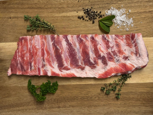 Raw pork ribs on a wooden surface with herbs and spices