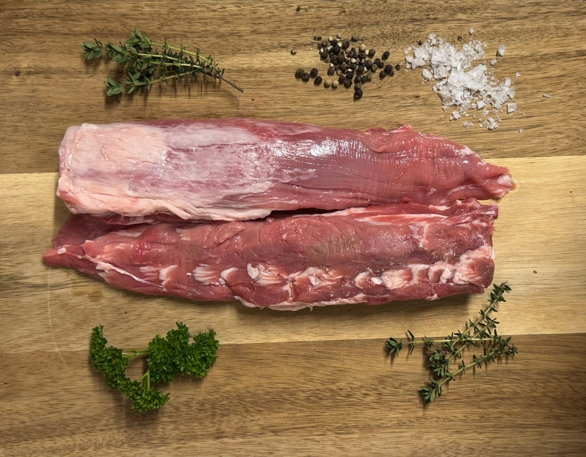 Two pieces of raw meat on a wooden cutting board with herbs and salt.