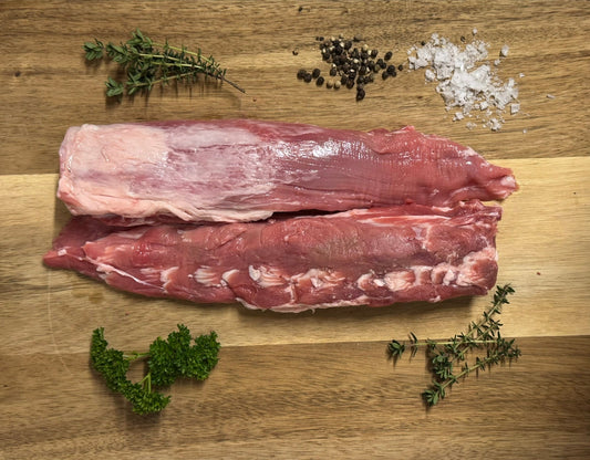 Two pieces of raw meat on a wooden cutting board with herbs and salt.